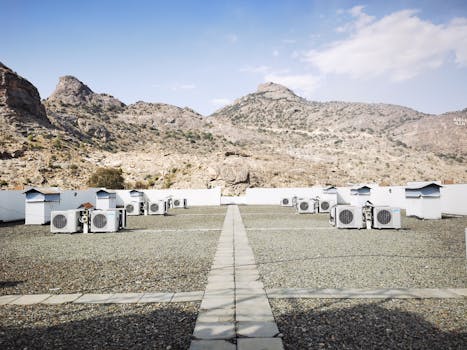 Rooftop air conditioning units on a gravel surface with a mountainous backdrop under a clear sky.